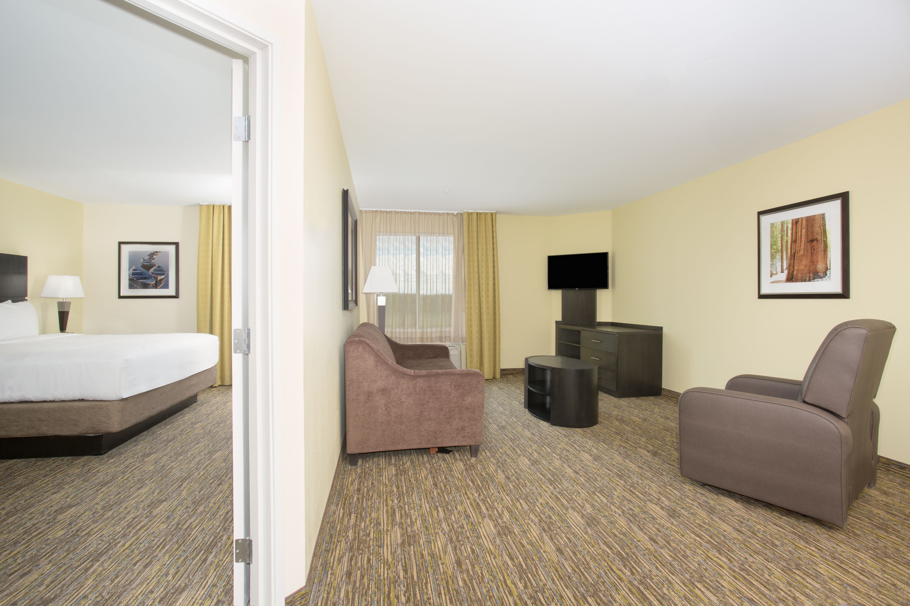 Ein Hotelzimmer mit einem Bett, zwei Sesseln, einem kleinen Tisch, einem Fernseher und einem gerahmten Bild an der Wand.