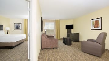 Ein Hotelzimmer mit einem Bett, zwei Sesseln, einem kleinen Tisch, einem Fernseher und einem gerahmten Bild an der Wand.