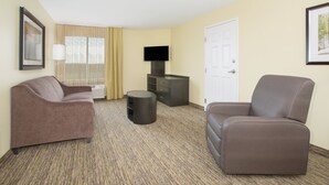 Una habitación de hotel con sofá, una silla, televisor, lámpara y puerta.