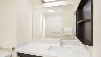 A bathroom with a white sink, a mirror, and a shower visible in the background.