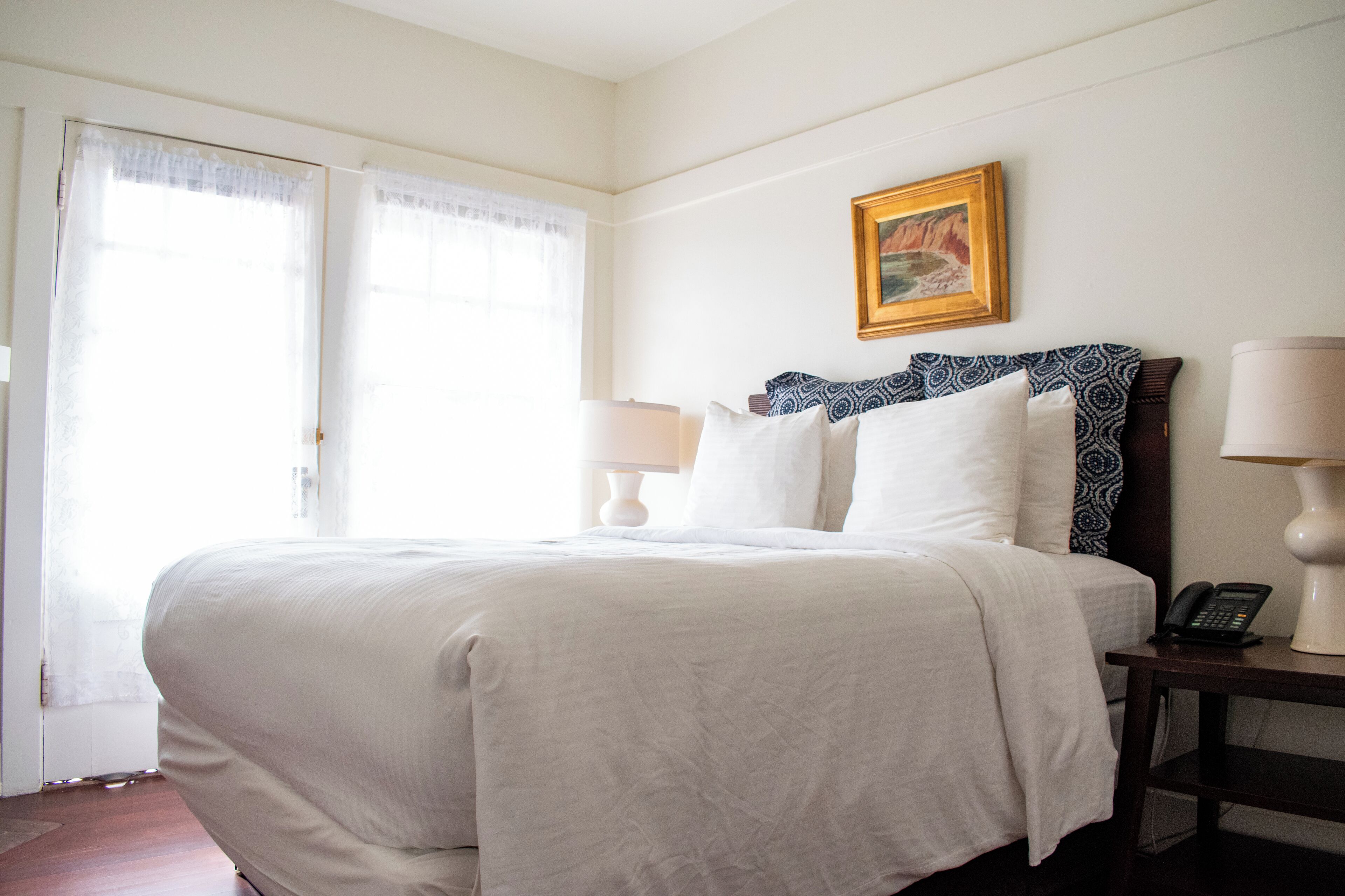 Habitación de hotel con una cama grande, una mesita de noche con lámpara, teléfono y un cuadro en la pared.