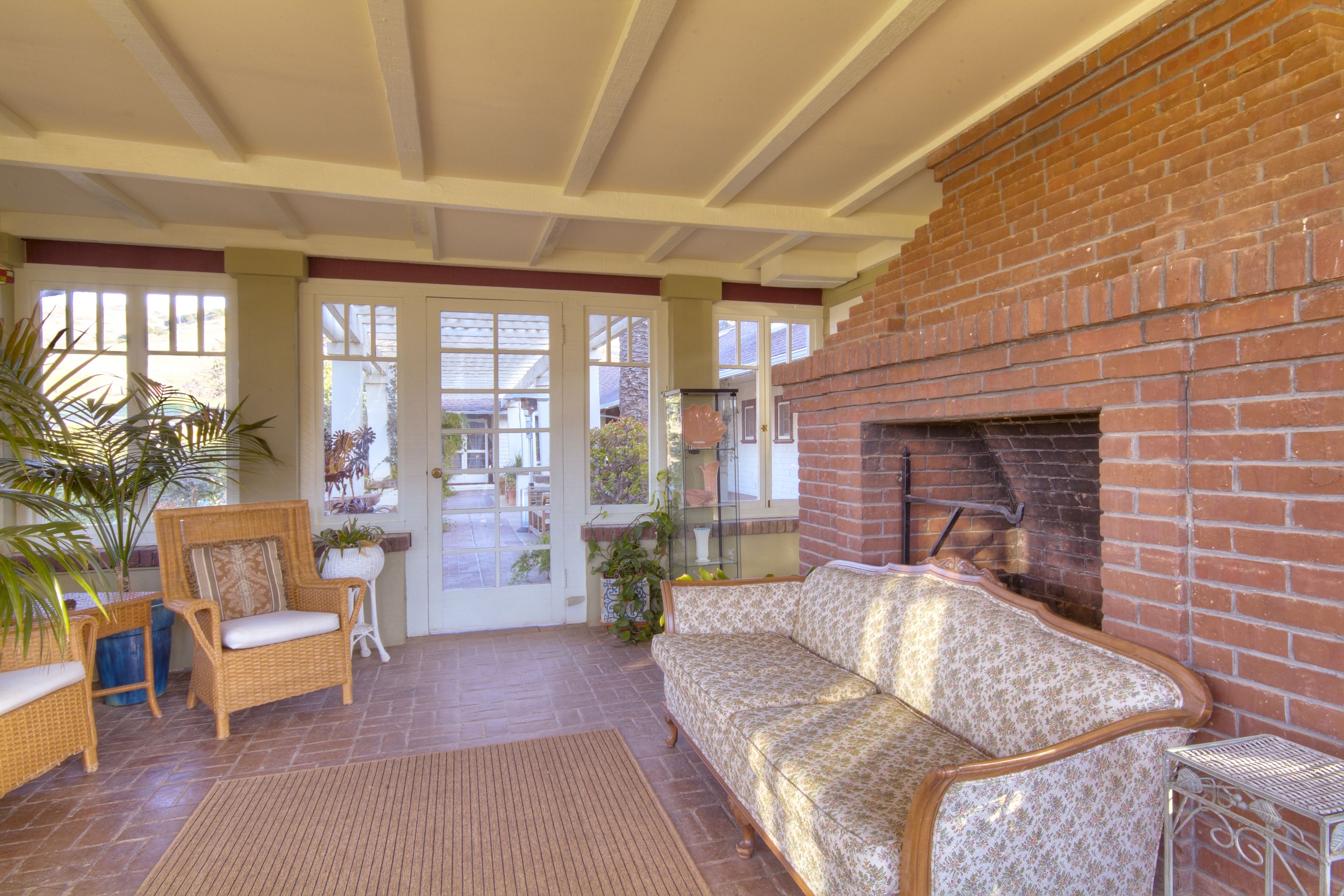 A covered patio area with wicker furniture, a brick fireplace, and a view of the outside.