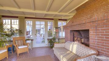 A covered patio area with wicker furniture, a brick fireplace, and a view of the outside.