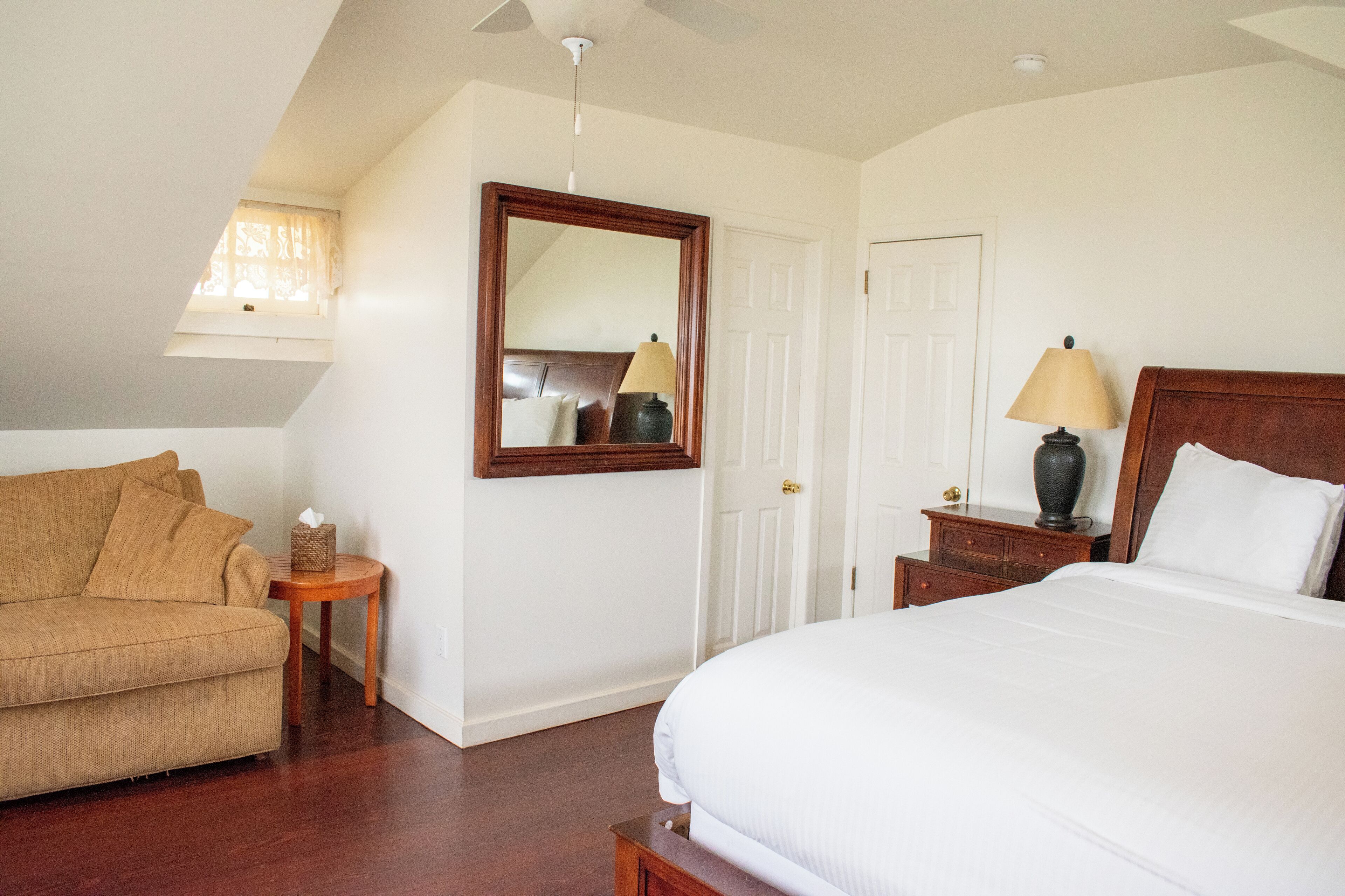 A bedroom with a bed, a nightstand, a lamp, a chair, a small table, and a mirror on the wall.