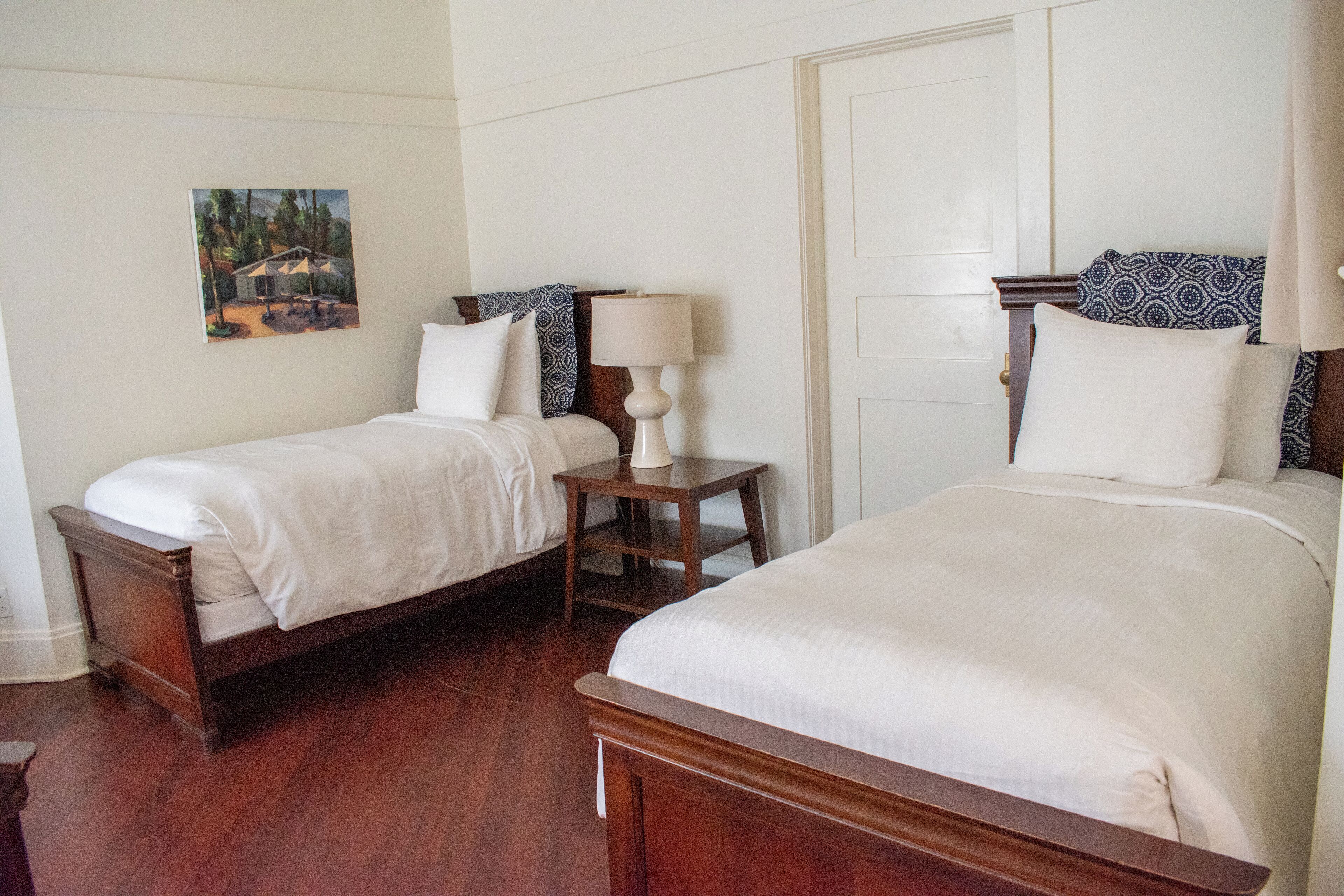 Two single beds with wooden frames, white bedding, and a small bedside table with a lamp.