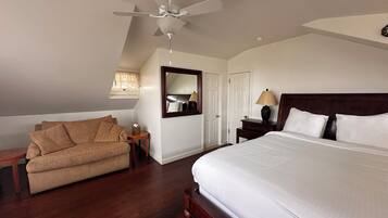 A bedroom with a large bed, a ceiling fan, a wooden nightstand, a lamp, a mirror, and a sofa.