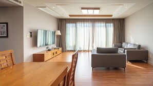 A modern living room with a wooden dining table, grey sofas, and a flat-screen TV mounted on the wall. - Elysian Gangchon Resort (Chuncheon)
