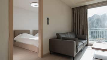 A hotel room with a bed, a sofa, a desk, and a balcony with a view of mountains.