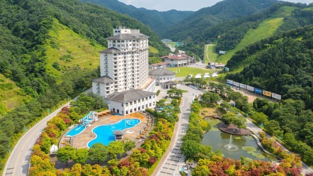 A hotel with a swimming pool, a small lake, and a mountainous backdrop. - Elysian Gangchon Resort (Chuncheon)