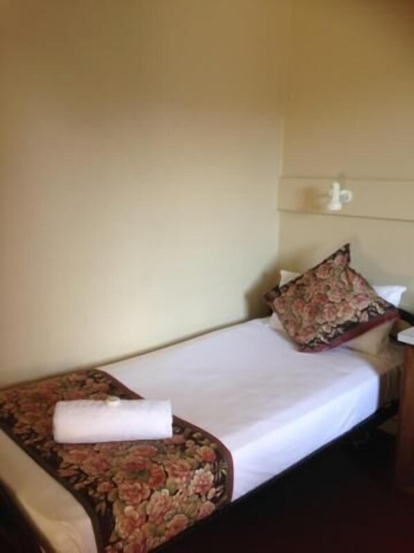Una cama individual con un edredón floral, una toalla blanca enrollada y una almohada a juego.