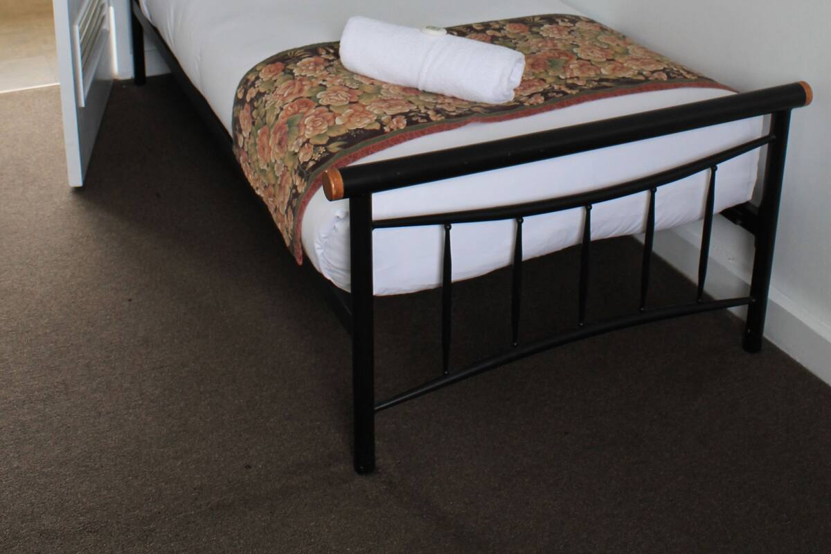 Una cama individual con una colcha estampada de flores, almohada negra y una toalla blanca al lado.