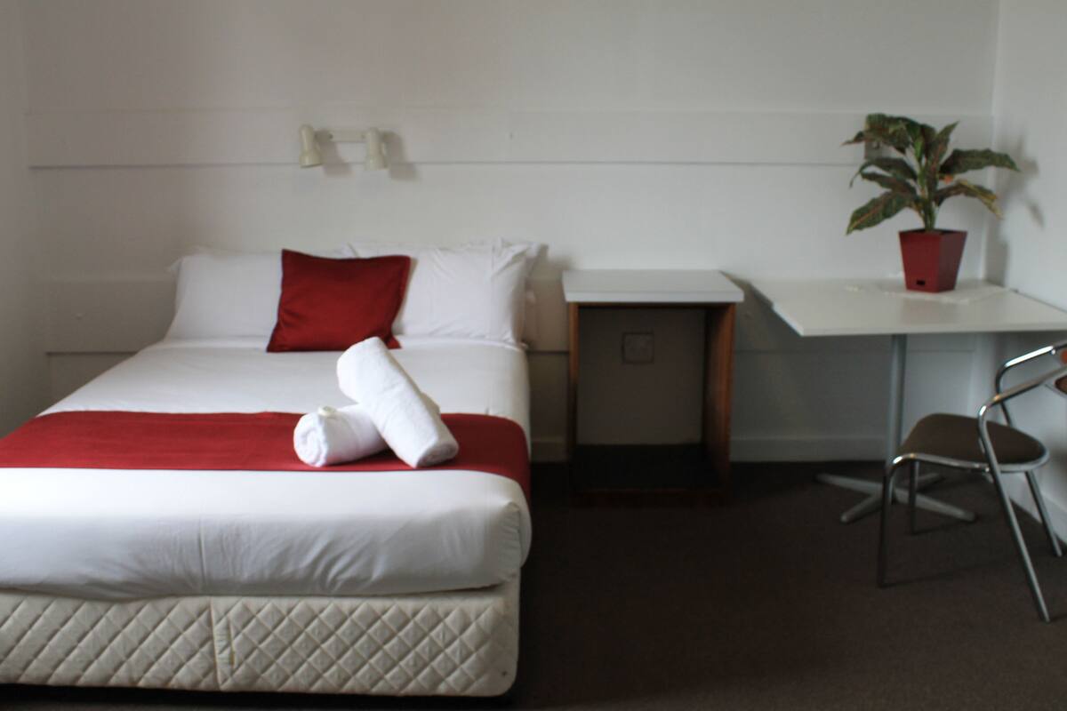 Habitación de hotel con cama, escritorio, silla y planta en maceta.