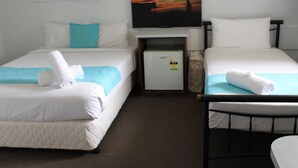 A hotel room with two beds, each with a white mattress and a blue blanket. There is a small refrigerator and a television on the wall. - Hotel Beach House Nambour (Nambour)