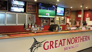 A Great Northern Brewing Co. counter with a fish logo, a TV screen displaying a sports game, and a sign for a game on 13/07. - Hotel Beach House Nambour (Nambour)