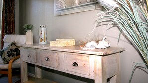 A wooden dresser with drawers, a vase with seashells, and a wall-mounted shelf with decorative items. - Pacific Palms Resort (Tauranga)