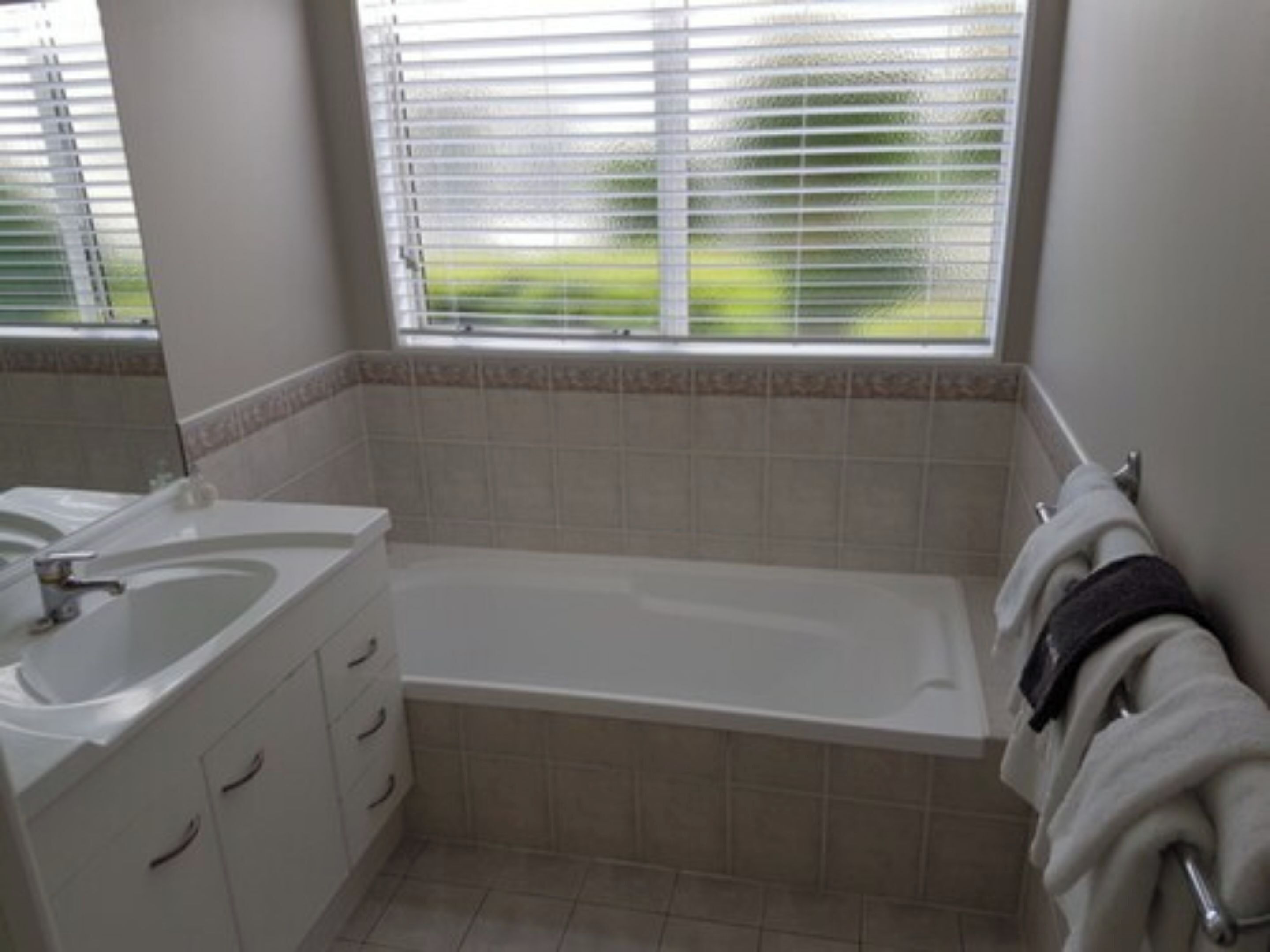Une salle de bain avec une baignoire, un lavabo et une fenêtre avec des stores.