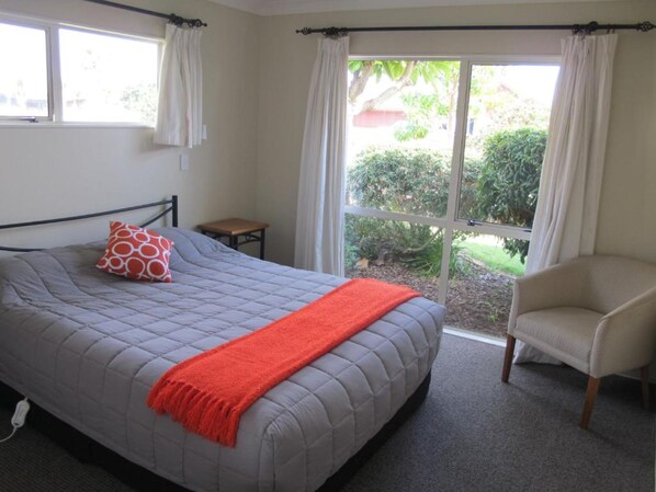 A bedroom with a bed, a chair, a small table, and a window with curtains.