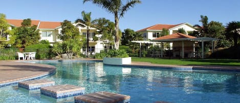 Una piscina al aire libre, sombrillas, sillones reclinables de piscina
