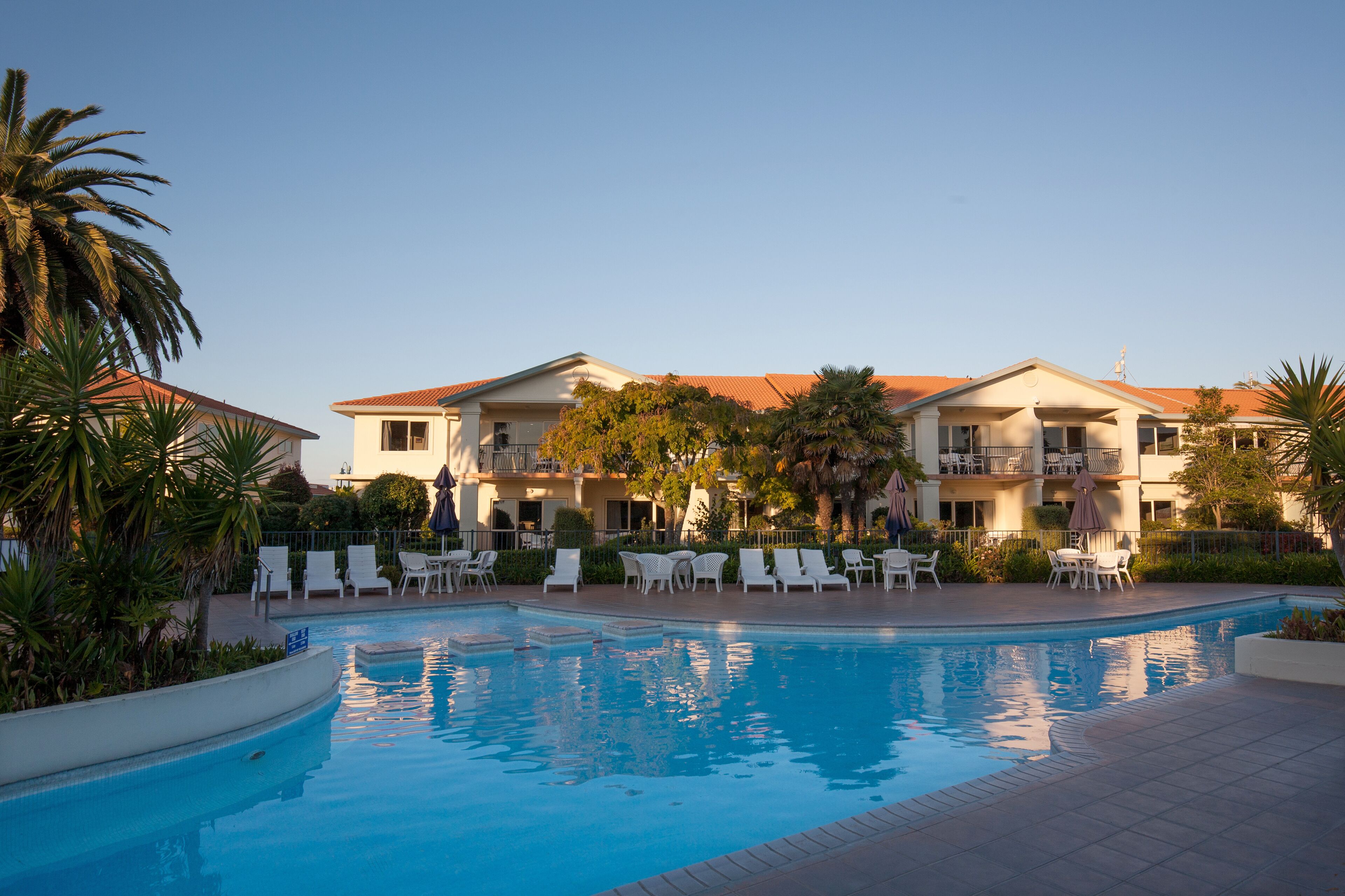 A hotel with a swimming pool, white lounge chairs, and palm trees.