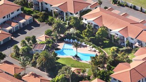 An aerial view of a resort with multiple buildings, a central swimming pool, and surrounding greenery. - Pacific Palms Resort (Tauranga)