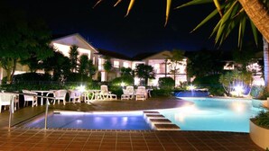 A swimming pool with lounge chairs and a building in the background. - Pacific Palms Resort (Tauranga)