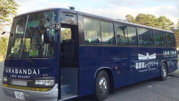 A blue bus with "URABANDAI LAKE RESORT" written on the side, parked on a road with trees in the background.