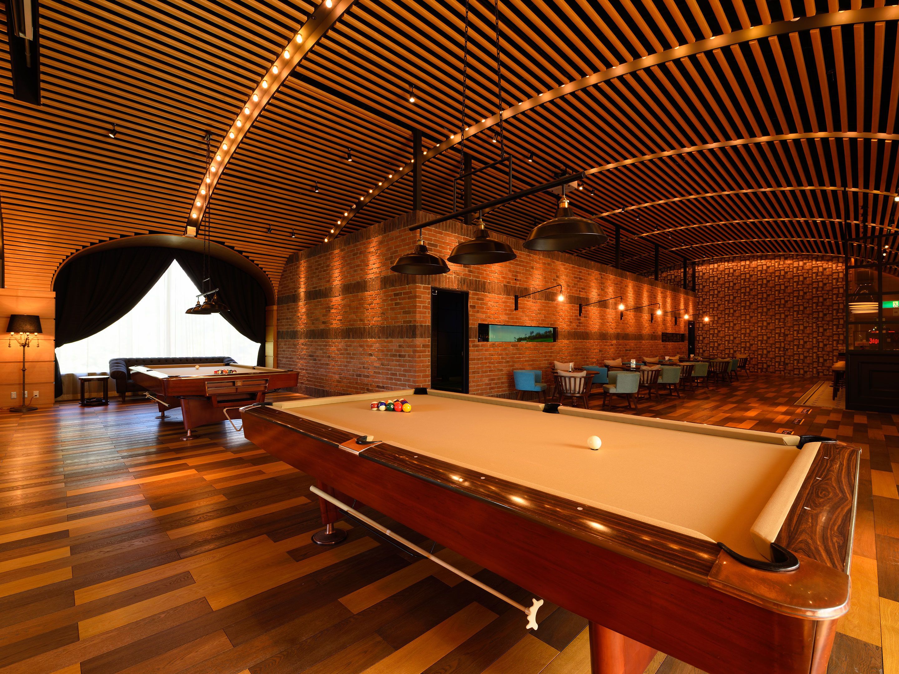 A pool table in a room with a wooden ceiling and brick walls.