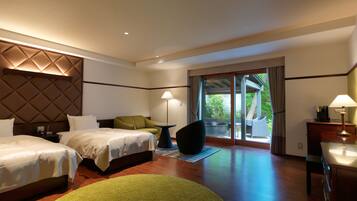 A hotel room with two beds, a green chair, a small table with a lamp, and a view of the outdoors through a sliding glass door.