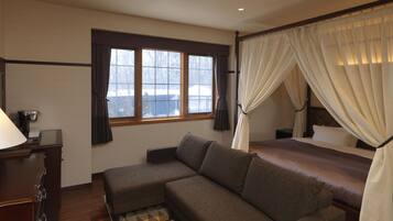 A bedroom with a sofa, a bed with a canopy, a desk with a lamp, and a window with curtains.