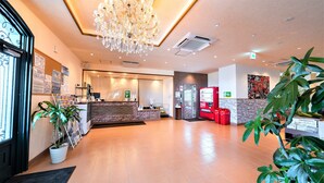 A hotel reception area with a chandelier, a reception desk, a red vending machine, and potted plants. - Hotel Castle Village Miyakojima (Miyakojima)
