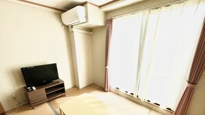 A room with a television on a wooden stand, a tatami mat, and a sliding glass door with curtains. - Hotel Castle Village Miyakojima (Miyakojima)