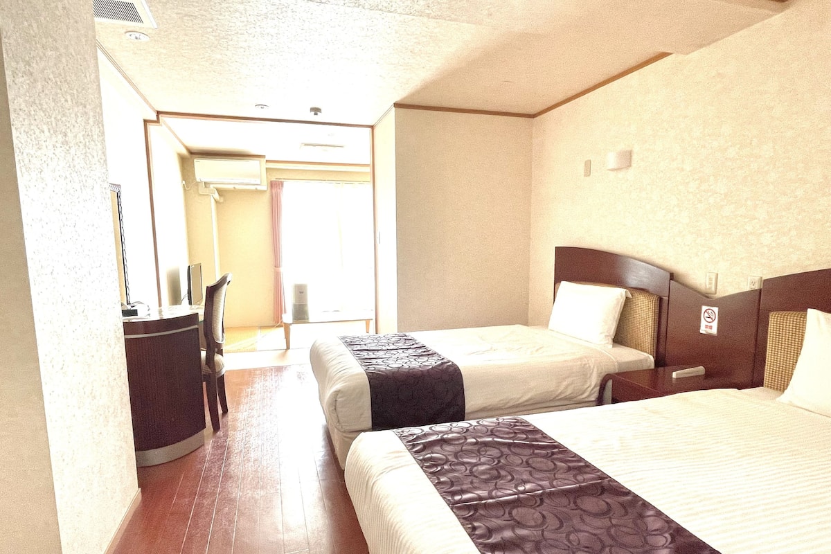 A hotel room with two beds, a desk, and a chair.