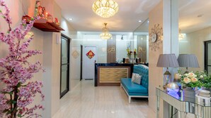 Um saguão de hotel moderno com um balcão de recepção, um sofá azul, lustres e elementos decorativos.
