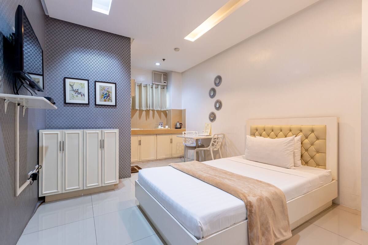 A modern bedroom with a bed, a desk, and a TV.