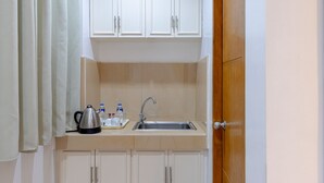 Uma cozinha pequena com armários brancos, uma pia e uma chaleira no balcão.