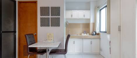 Cocina compacta con armarios blancos, un lavamanos y una ventana. Hay una mesa de comedor con dos sillas.