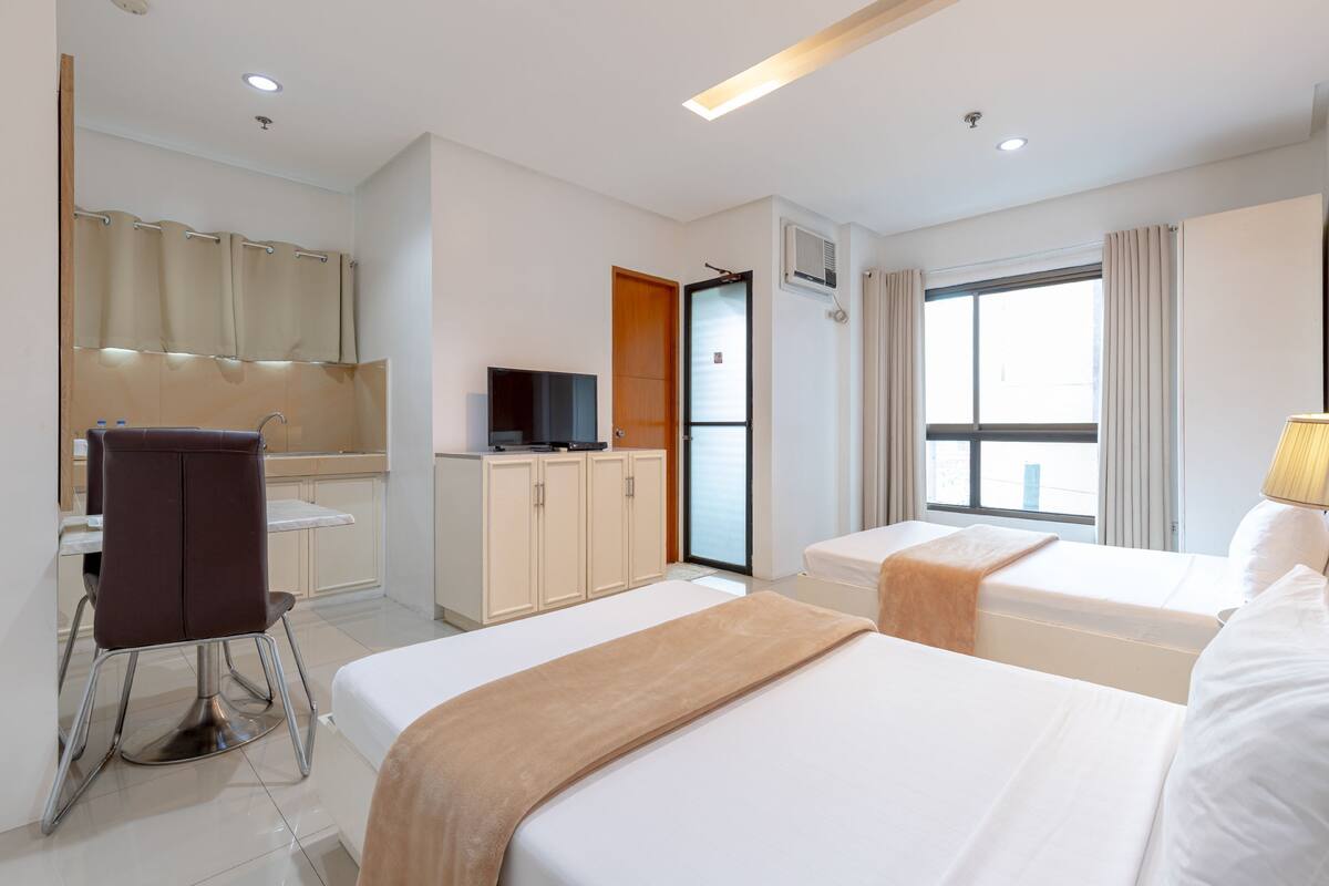 A hotel room with two beds, a desk, a chair, a TV, and a window with curtains.