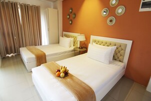 A hotel room with two beds, a bedside table with a lamp, and a fruit basket on the bed.