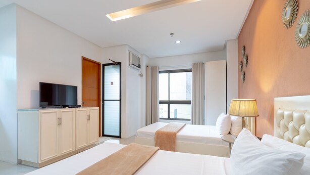 Quarto de hotel com duas camas, televisão, abajur e janela com cortinas.
