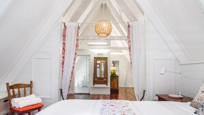 Ett sovrum med en stor säng, en trästol, ett sängbord och en hängande lampa.