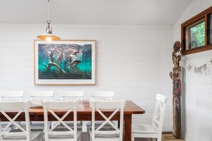 A dining area with a wooden table and white chairs, a framed artwork above the table, and a decorative wall piece. - A PERFECT STAY - Longhouse (Byron Bay)