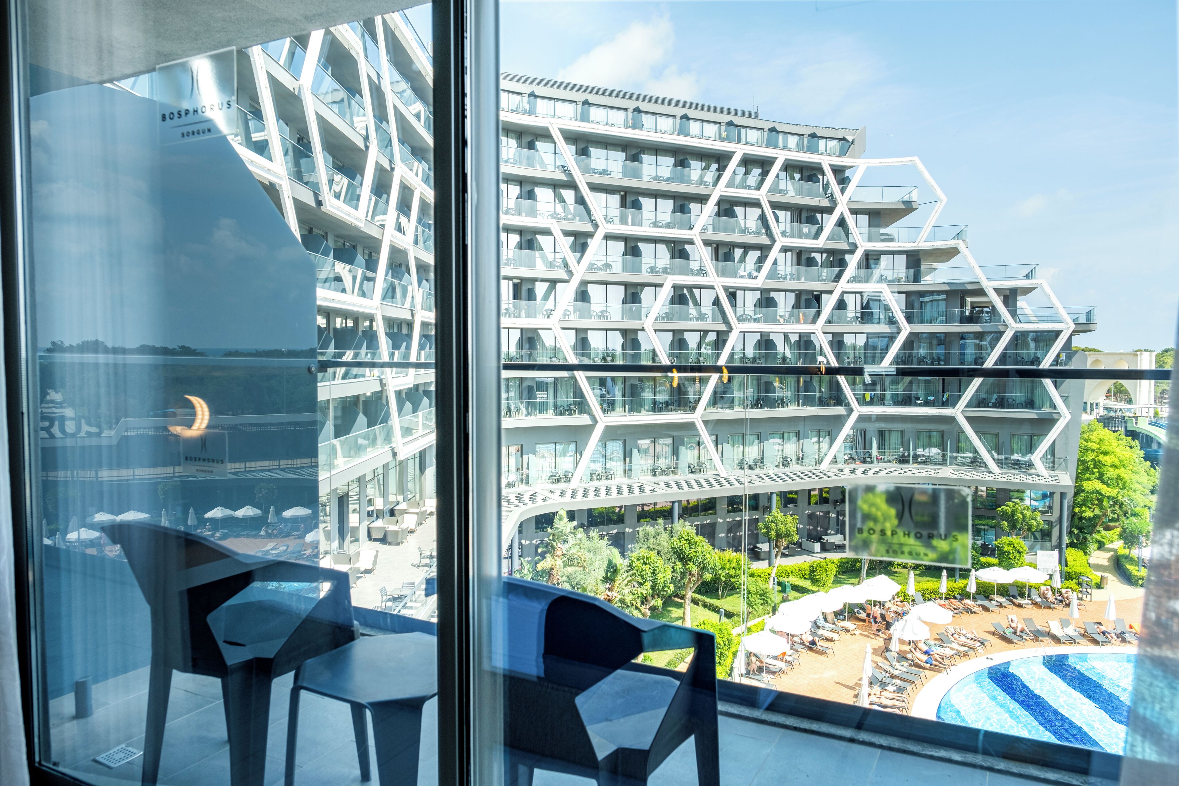 A modern building with a geometric facade and a pool area visible through the window.