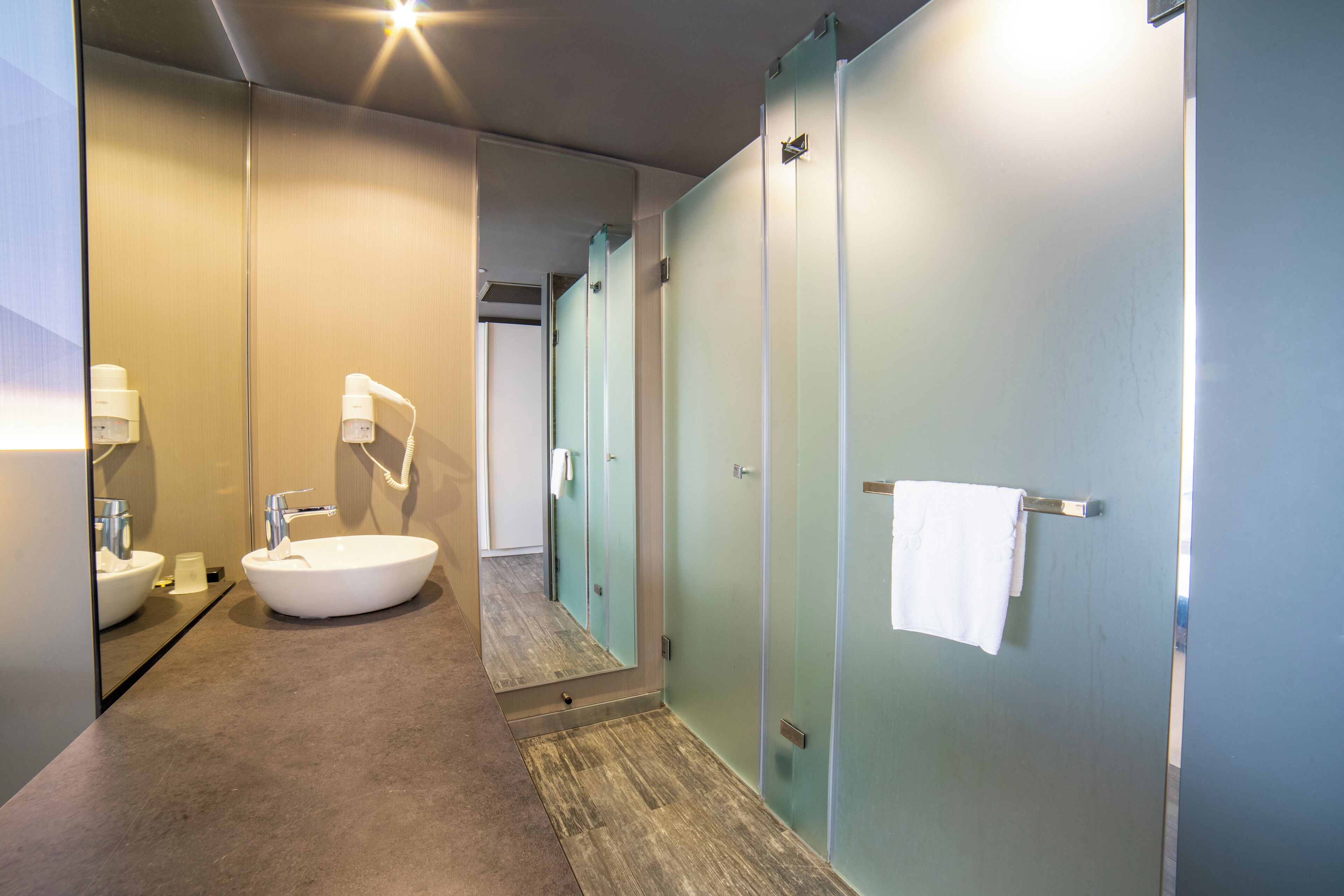 Een moderne badkamer met een groot wastafelmeubel, spiegel en douchedeuren van glas.