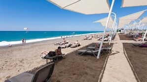 Una playa con tumbonas y sombrillas, cielo azul despejado y el océano al fondo.