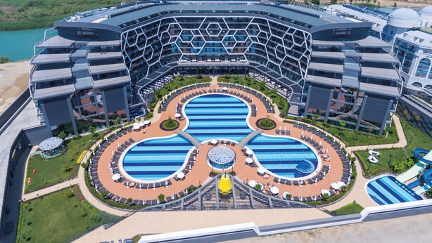 Un hotel moderno con un área de piscina central, varias piscinas y una gran estructura de edificio.