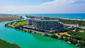A modern hotel with a hexagonal facade, situated by a river with boats docked nearby. - Bosphorus Sorgun Hotel - All Inclusive (Manavgat)