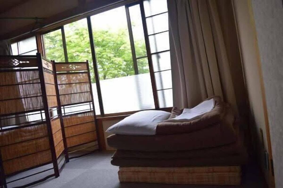 A room with a bunk bed, a window with curtains, and a view of greenery outside.