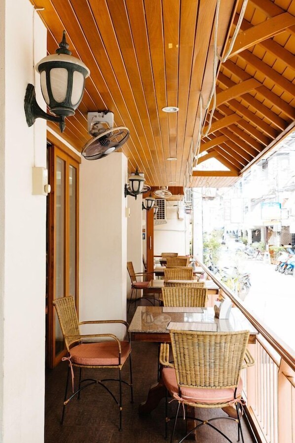 An indoor seating area with wicker chairs and tables, wooden ceiling beams, and wall-mounted lamps. - Thipurai Beach Hotel (Hua Hin)