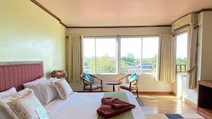 A hotel room with a large bed, two chairs, a small table, and a view of greenery outside. - Thipurai Beach Hotel (Hua Hin)