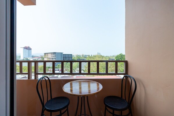 En balkon med to stole og et rundt bord, udsigt over bybilledet med bygninger og grønne områder.